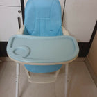 Blue baby high chair with white legs on a tiled floor.