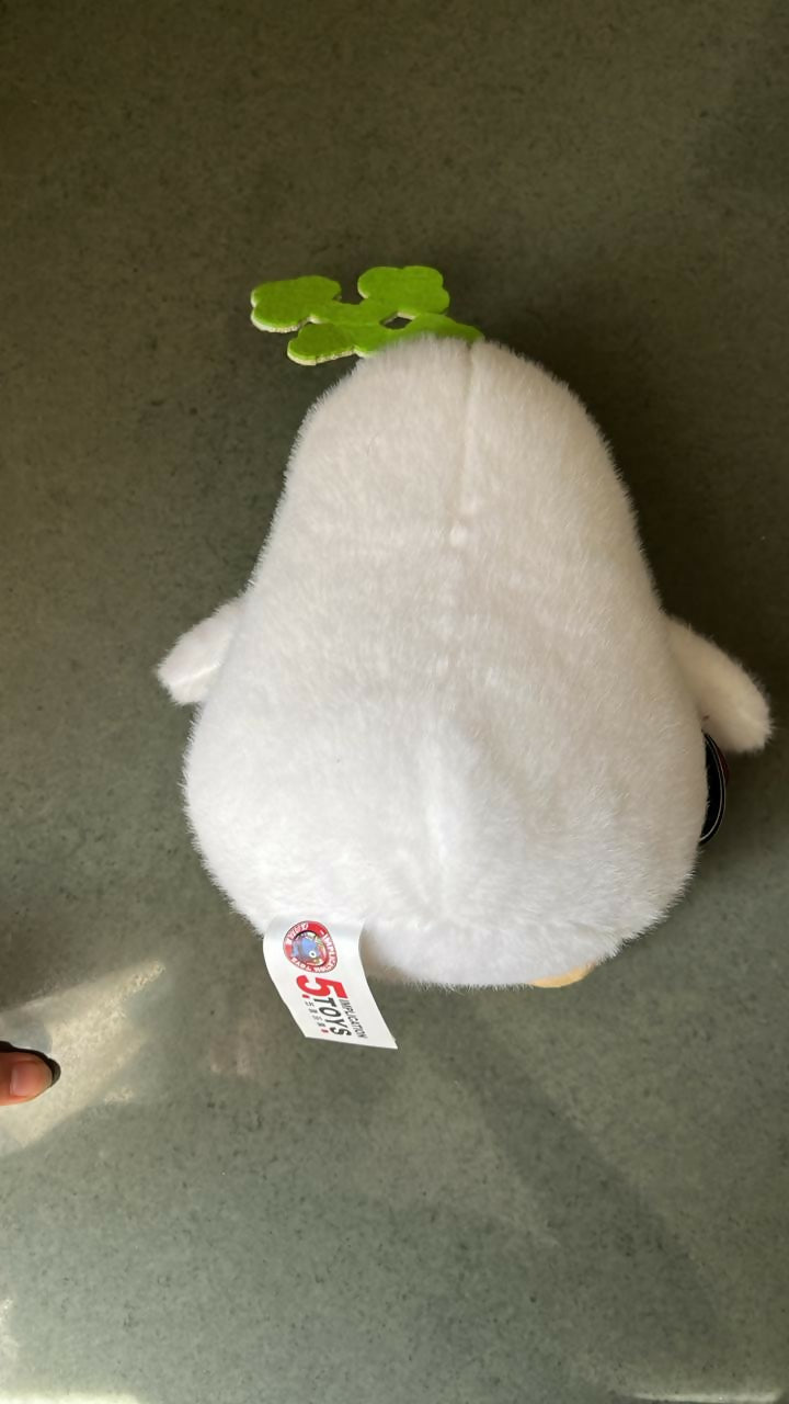 White plush toy with a green leaf on a gray surface
