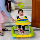 Child using a yellow and green walker with a person assisting, indoors.