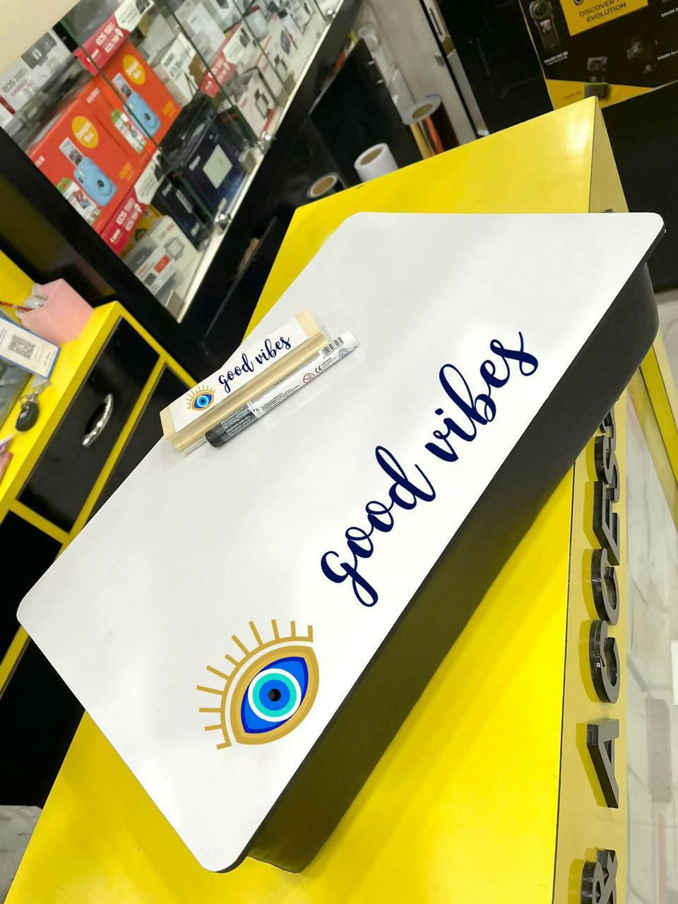 White board with 'good vibes' text and eye design on a yellow surface