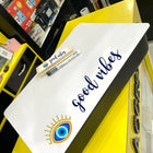 White board with 'good vibes' text and eye design on a yellow surface