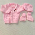 Pink baby cardigan, hat, and booties set on a textured surface