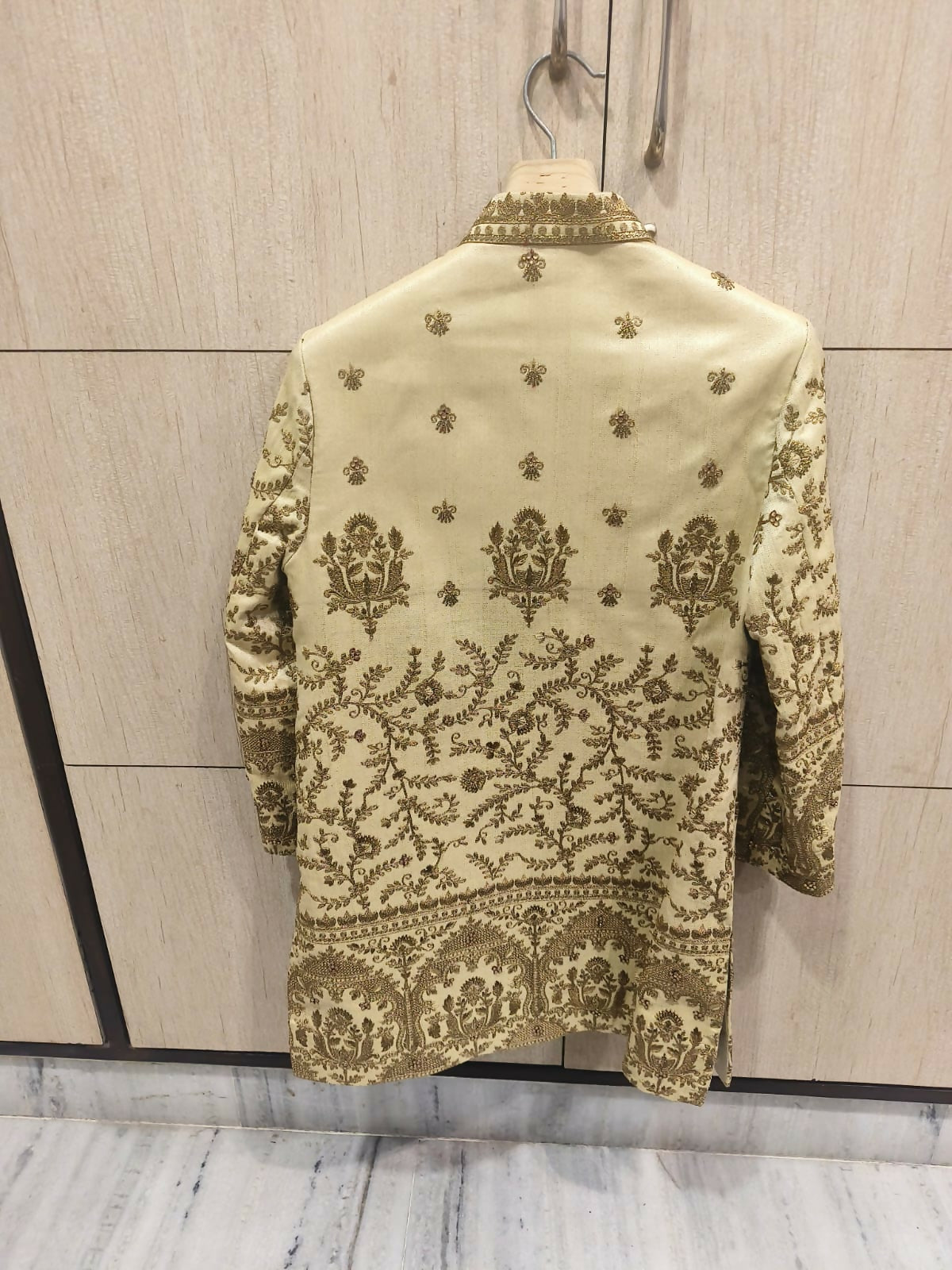 Embroidered traditional jacket on a hanger against a light wooden panel background
