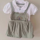Children's outfit with white shirt and green overalls on a hanger against a beige background