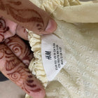 Henna-decorated hand holding a cream-colored garment with an H&M tag.