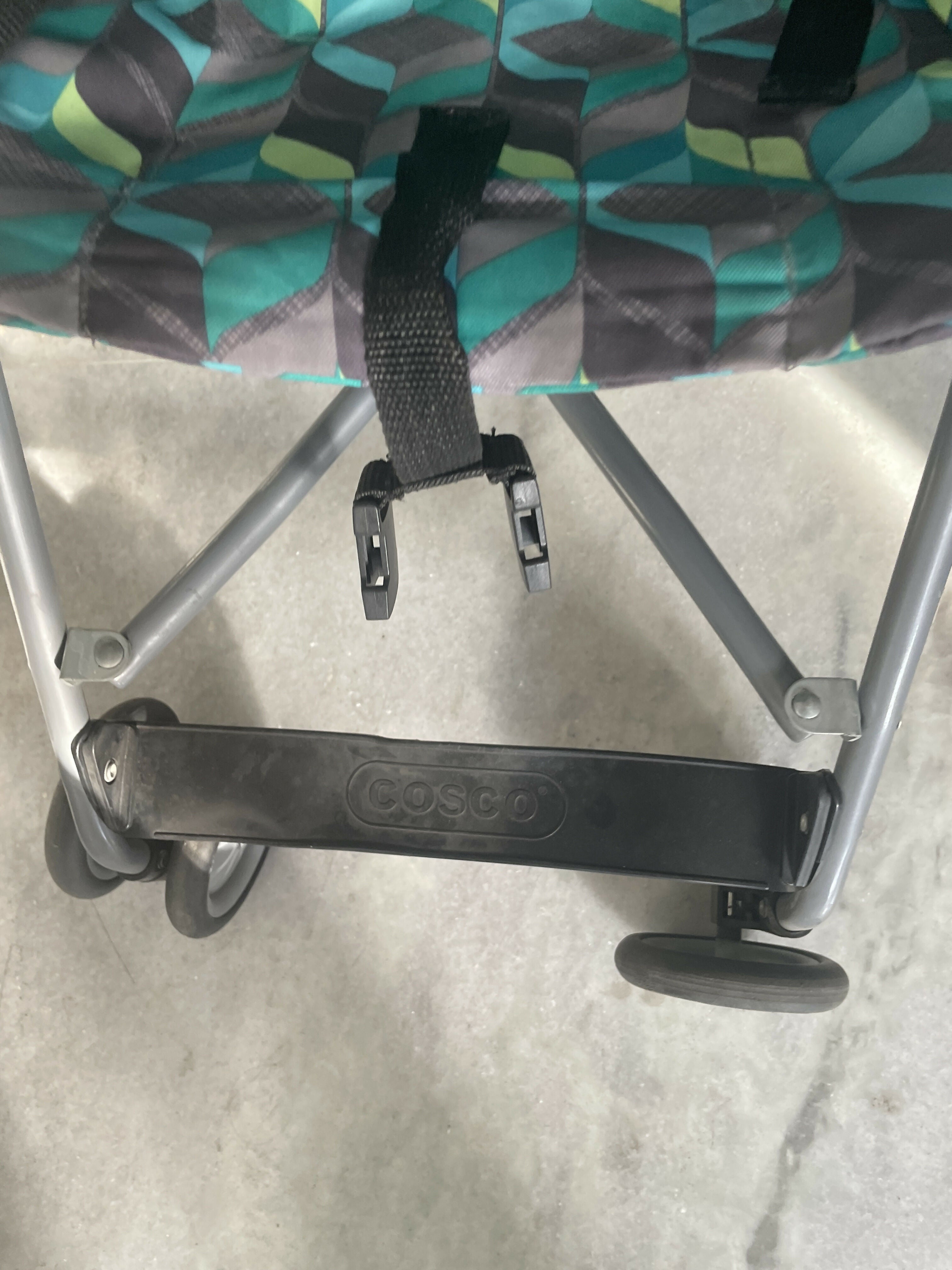 Close-up of a Cosco stroller seat with a patterned cover on a concrete surface.