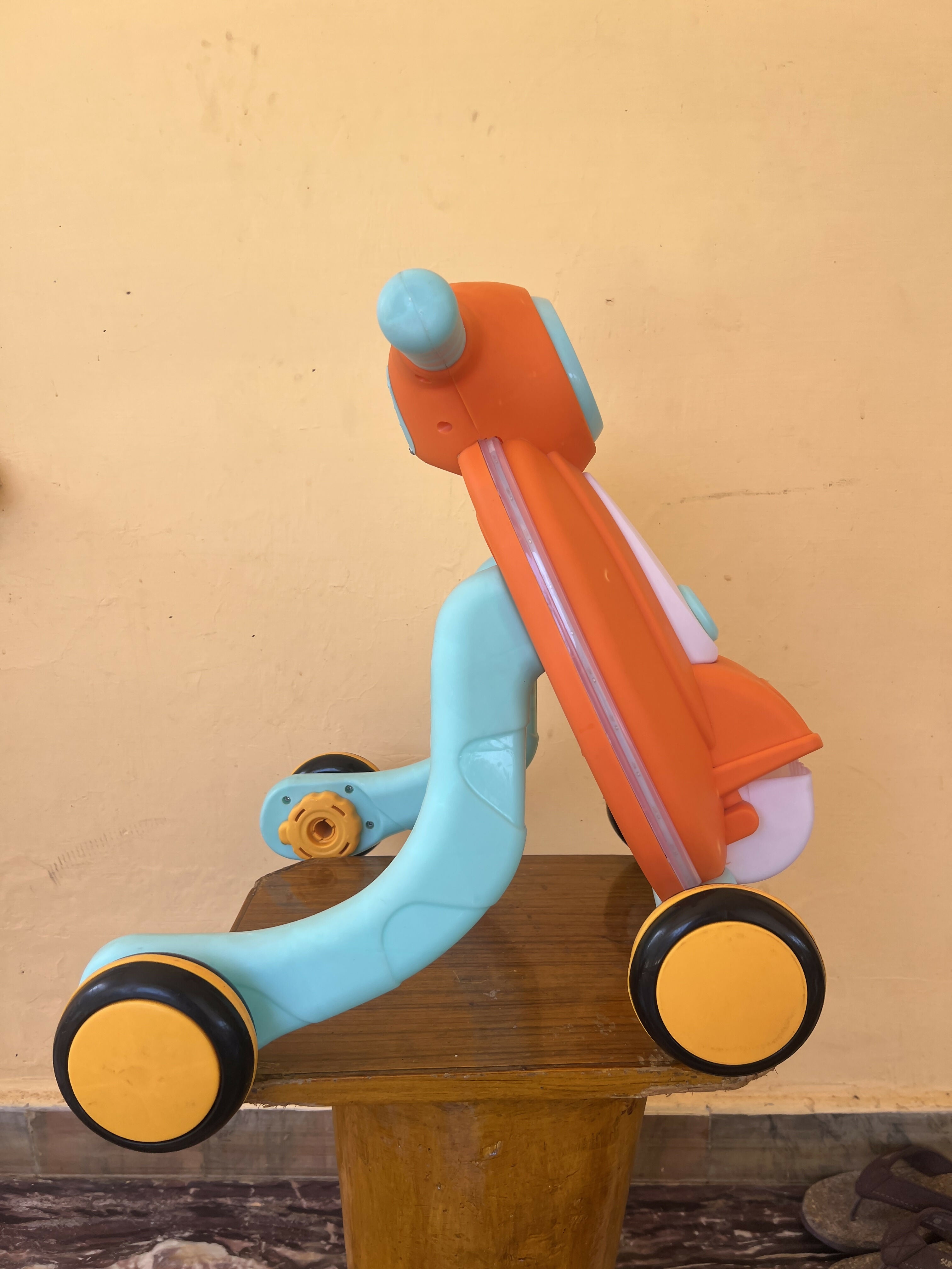 Children's multicolored scooter on a wooden surface with a beige wall background
