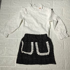 White blouse with long sleeves and a black skirt with white patterns 