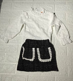 White blouse with long sleeves and a black skirt with white patterns 