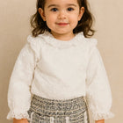 Young girl wearing a white blouse with ruffled details and a patterned skirt 