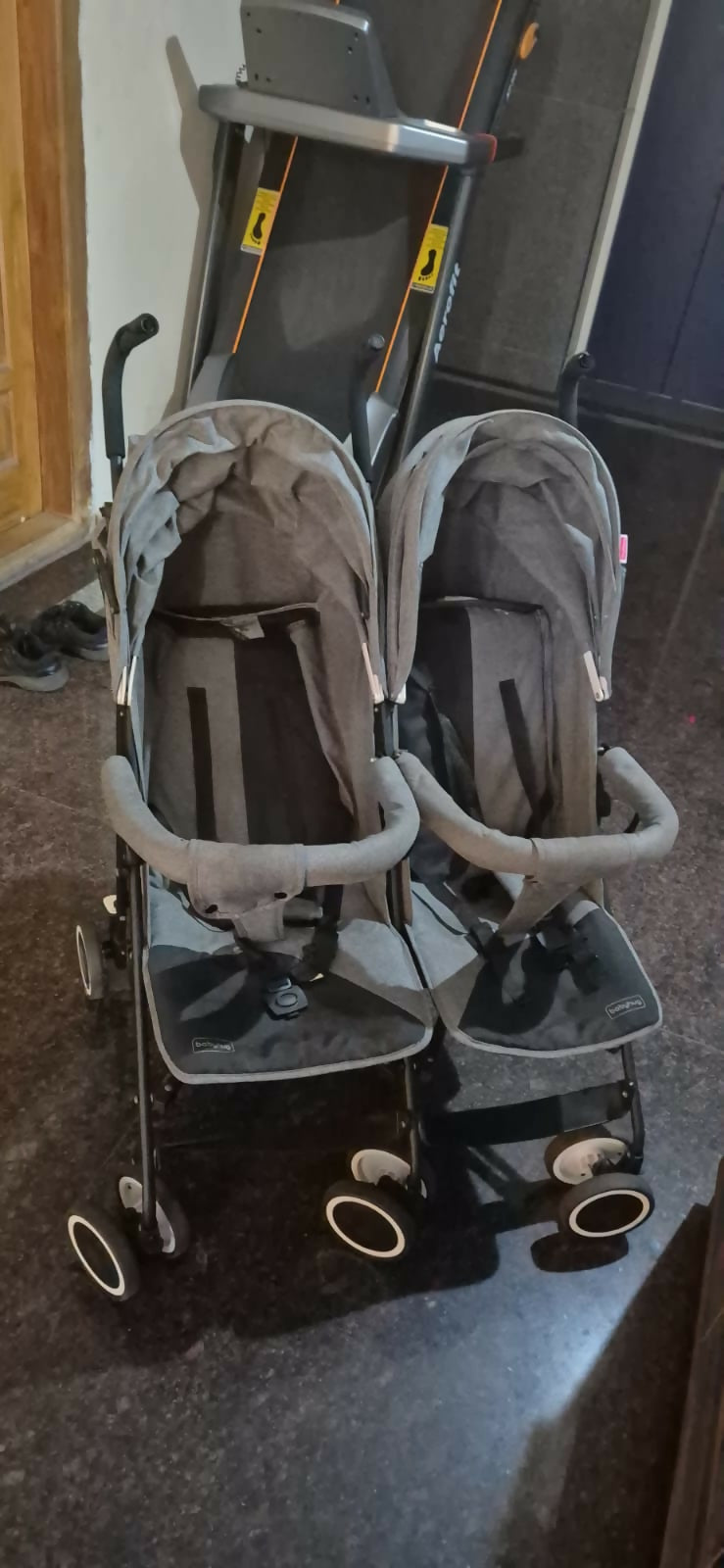 Double stroller with gray covers on a dark floor.