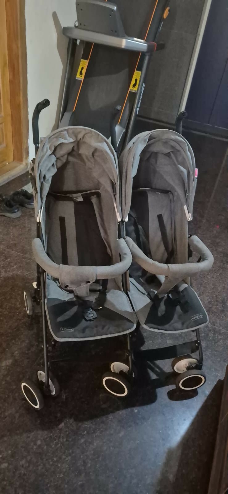 Double stroller with gray covers on a dark floor.