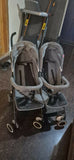 Double stroller with gray covers on a dark floor.