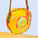 Yellow crossbody bag with rainbow design and text on a light blue background