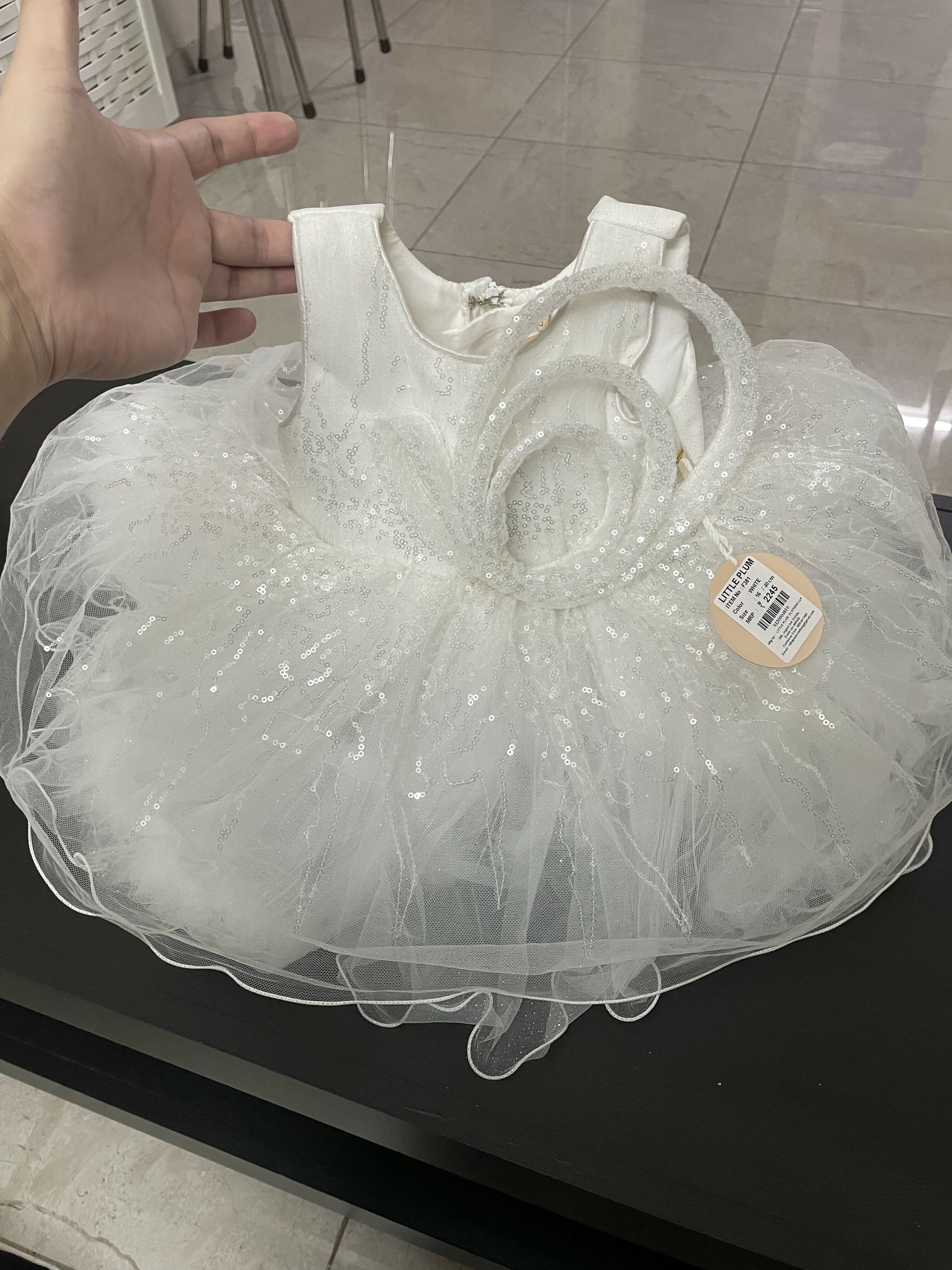 White dress with a sheer overlay on a black surface, held by a hand.