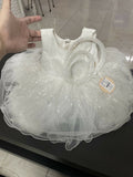 White dress with a sheer overlay on a black surface, held by a hand.