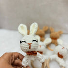 Hand holding a white crochet bunny with wooden teethers on a light background